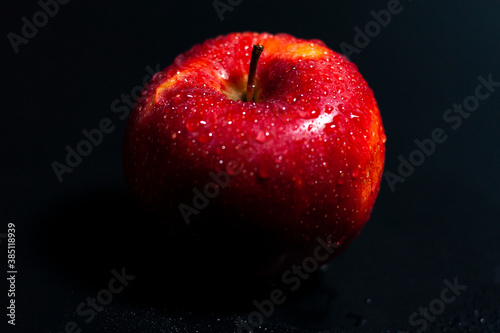 Fresh Apple of dark red color with water droplets. In the center of the screen.