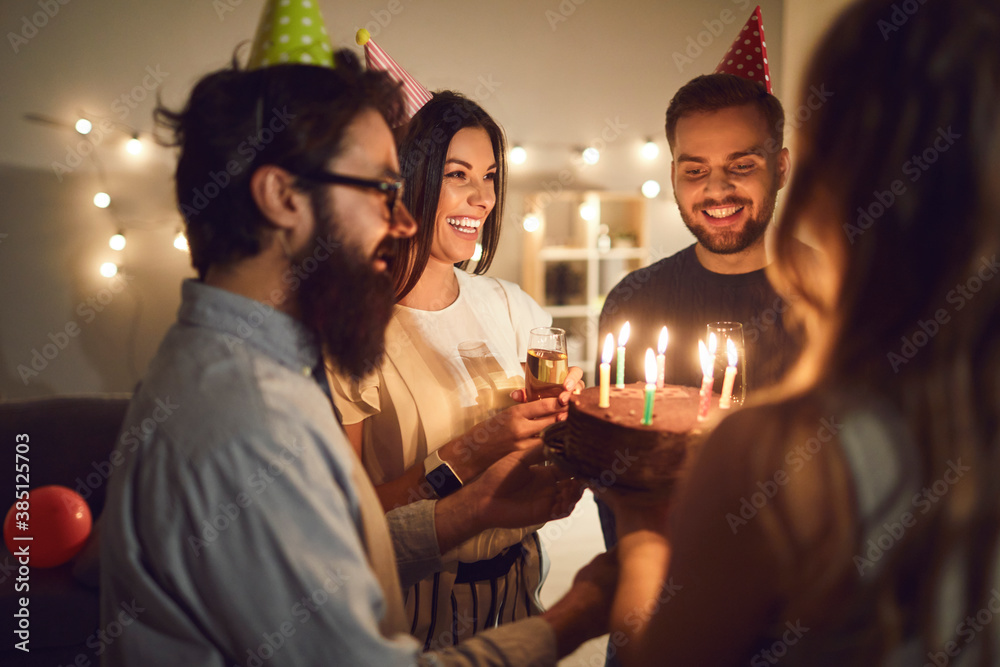 Group of smiling friends presenting birthday cake to their friend