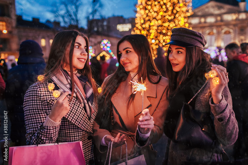New Year and Christmas. Women friends burning sparklers in Lviv by Christmas tree on street fair. Girls celebrating