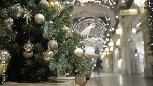 Christmas tree decorated with different Golden balls. People walk by in out of focus