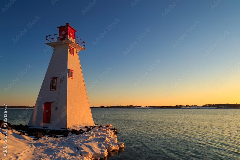 Red and white lighthouse looking out on a flowing lake during a warm, winter, sunset with clear skies, in Charlottetown Prince Edward Island, Canada