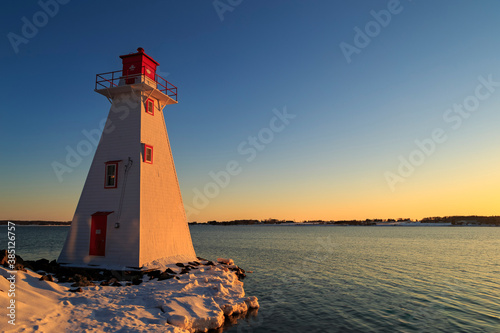 Red and white lighthouse looking out on a flowing lake during a warm, winter, sunset with clear skies, in Charlottetown Prince Edward Island, Canada photo