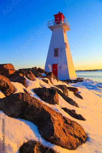 Red and white lighthouse looking out on a flowing lake during a warm, winter, sunset, with clear skies, in Charlottetown Prince Edward Island, Canada