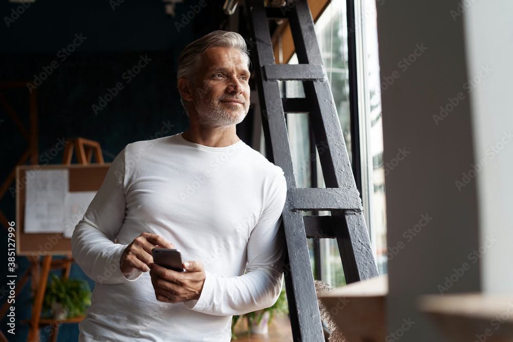 Business lifestyle. Casual Grey-haired Mature professional handsome businessman standing near window in his office while thinking about his goals Business lifestyle. Casual Grey-haired Mature professional handsome businessman standing near window in his office while thinking about his goals