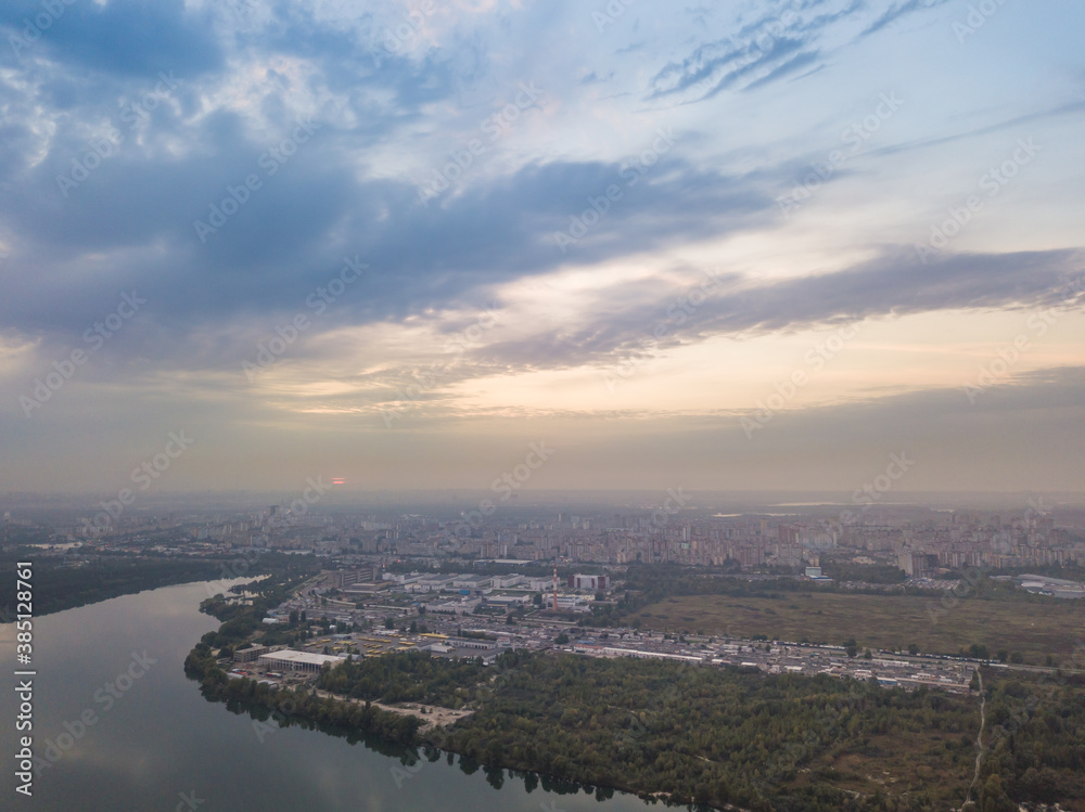 Aerial drone view. Lake on the outskirts of the city. The lake reflects the sky in the rays of the sunset. Cloudy.