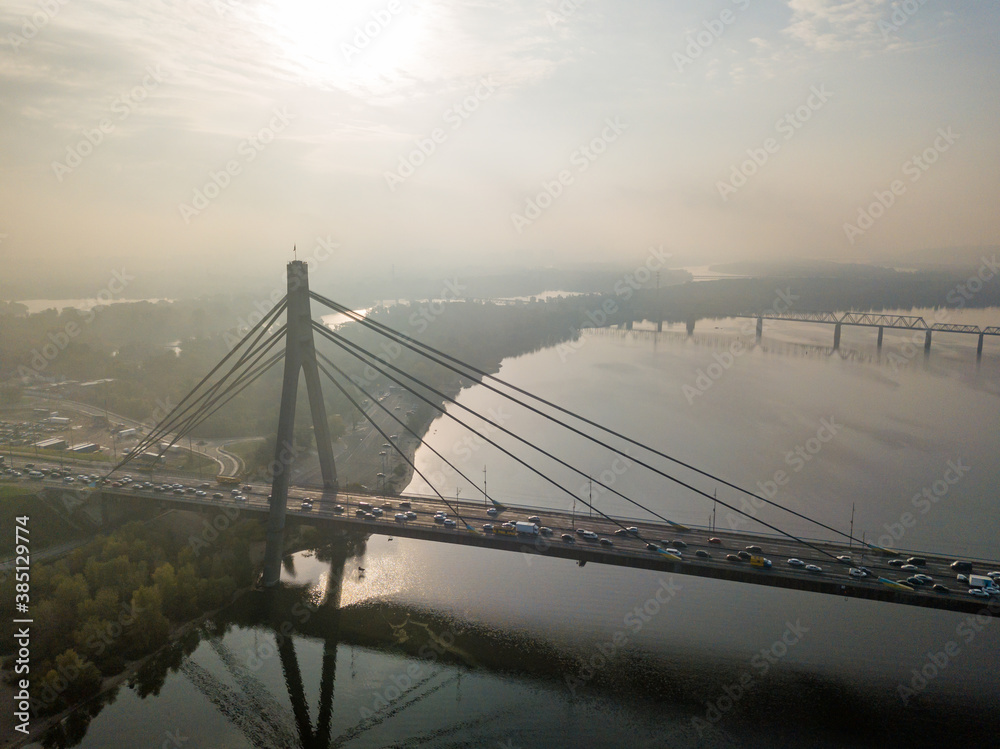 Fototapeta premium Aerial drone view. North bridge in Kiev in the rays of a sunny morning. Autumn haze in the air, cars are driving across the bridge.