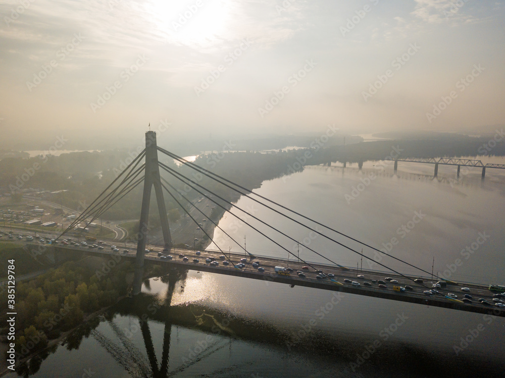 Obraz premium Aerial drone view. North bridge in Kiev in the rays of a sunny morning. Autumn haze in the air, cars are driving across the bridge.