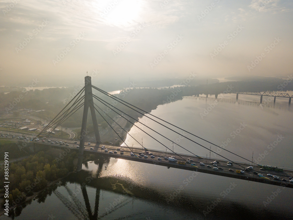 Obraz premium Aerial drone view. North bridge in Kiev in the rays of a sunny morning. Autumn haze in the air, cars are driving across the bridge.