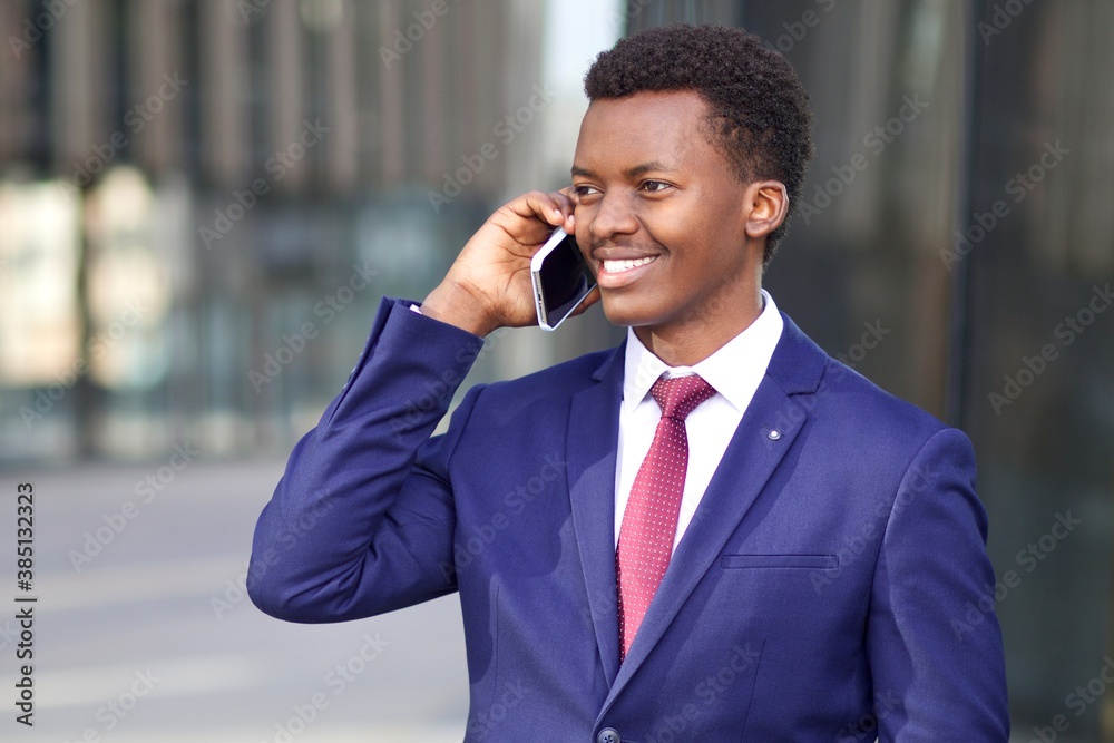 Portrait of happy positive young businessman in formal suit talking on his cell mobile phone. Black African Afro American man calling, having conversation on his smartphone and smiling Portrait of happy positive young businessman in formal suit talking on his cell mobile phone. Black African Afro American man calling, having conversation on his smartphone and smiling