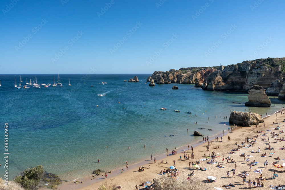 Crowded beach on the Algarve coast. Group of boats out in the ocean. Lagos, Portugal