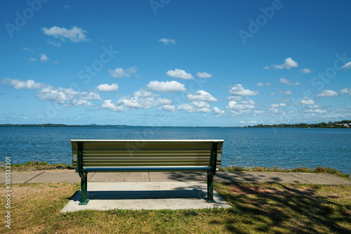 A place to sit and relax. Bench seat beside the water, with a view across the bay to islands on the horizon, and blue sky with fluffy clouds. Victoria Pt, Moreton Bay, Redlands, Queensland, Australia. © Silky Oaks