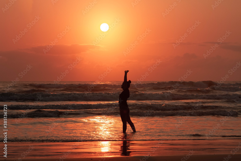 a silhouette of young beautiful girl looking to a perfect sunrise in the background 