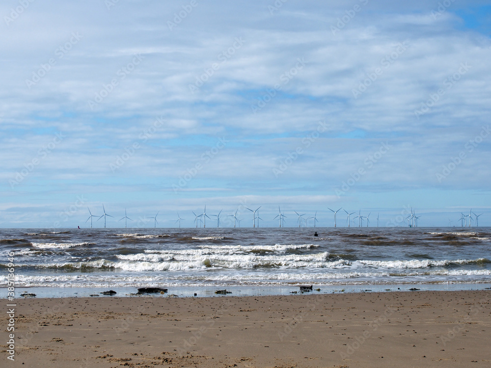 the beach at blundell flats in southport with waves braking on the beach and the wind turbines at burbo bank visible in the distance