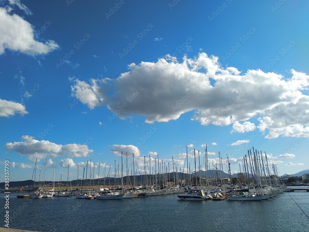 Seascape in Sardinia, sailing boats in the harbor and clouds Seascape in Sardinia, sailing boats in the harbor and clouds