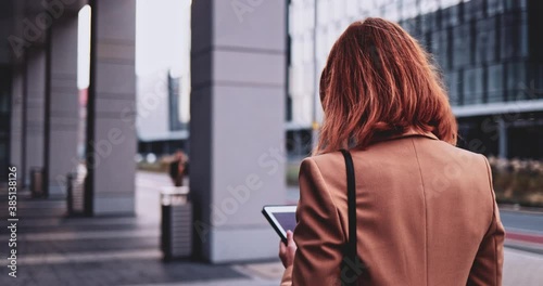 Business Woman Using Digital Tablet Walking In City. SLOW MOTION Gimbal Stabilized. Female entreprneur networking in internet, typing, texting, learning online, rushing to the office in the morning.  photo