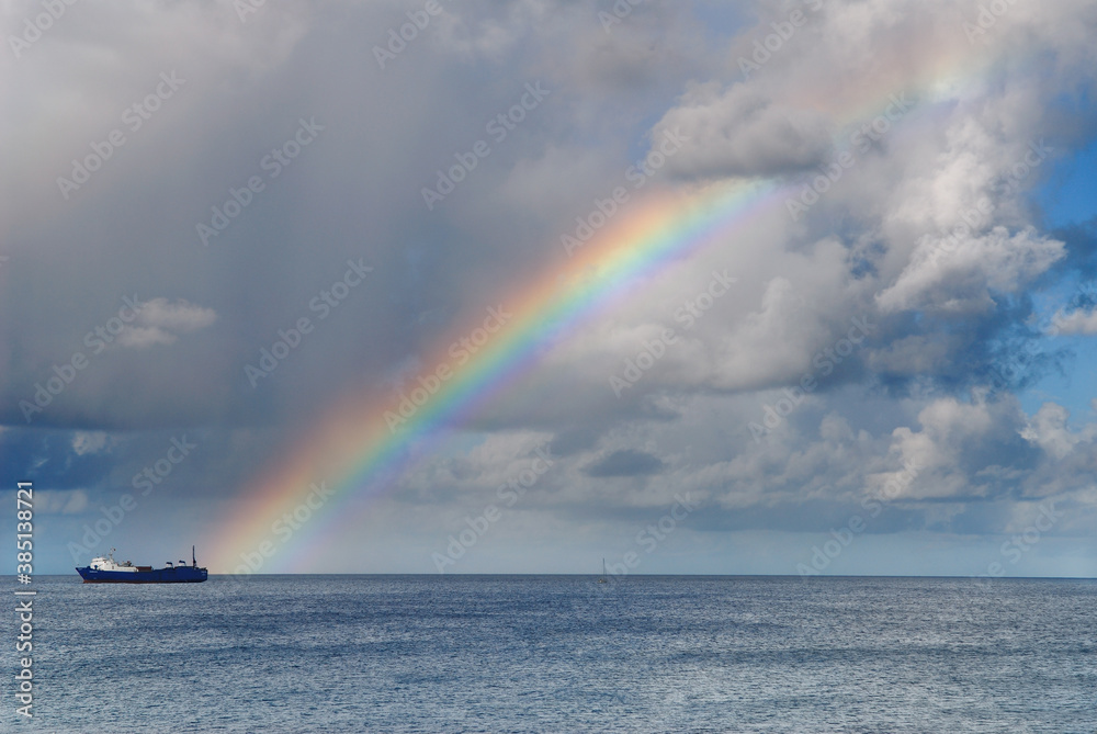 Rainbow over the Caribbean Sea ending at a freighter