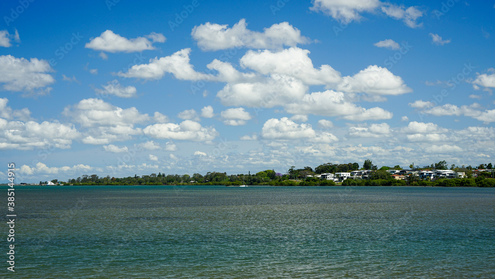 Clouds over the bay. View across the water from Victoria Point to houses and trees along the waterfront at Redland Bay, Queensland, Australia. 