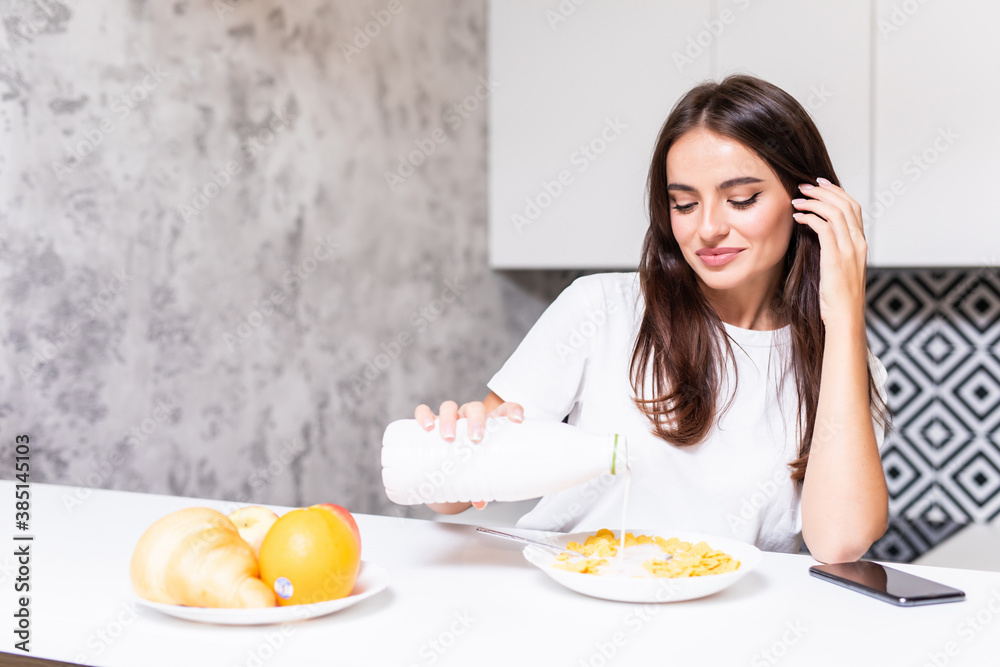 Smiling happy woman having a relaxing healthy breakfast at home sitting at kitchen table eating cereals wtih fruit and yogurt