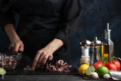 Close-up view of professional chef cuts octopuses for cooking, on the background of vegetables on a dark blue background. Asian cuisine. Traditional recipe. Seafood concept. Backstage of preparing