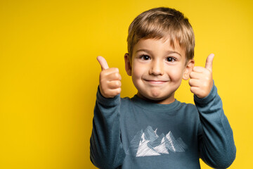 Portrait of happy small caucasian boy in front of yellow background thumbs up - Childhood growing up and achievement concept - front view waist up copy space