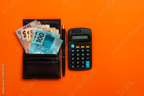 Brazilian money in wallet, with notepad, pen and calculator. Finance and salary concept. Economy of Brazil. Orange background