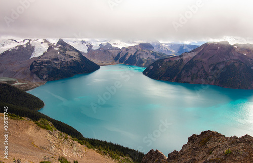 Panorama Ridge trail in Garibaldi Provincial Park, BC. The aerial view on turquoise lake surrounded by snowy mountains. Cloudy sky.