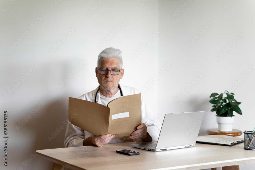 Senior doctor examining medical record while sitting at desk in clinic Senior doctor examining medical record while sitting at desk in clinic