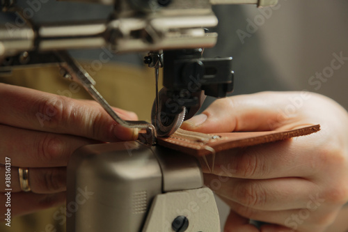 Tailor diligently sewing leather on sewing machine under lamp photo