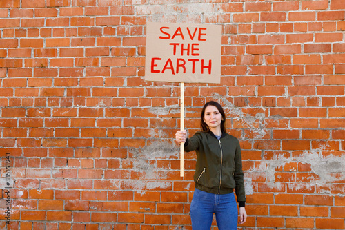 Young woman showing ecological banner against brick wall photo