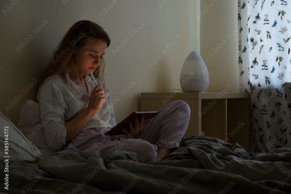 Thoughtful adult female student interacting with digital tablet using pen in cozy bedroom Thoughtful adult female student interacting with digital tablet using pen in cozy bedroom
