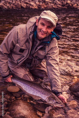 Smiling fly fisherman holding caught salmon fish in river
