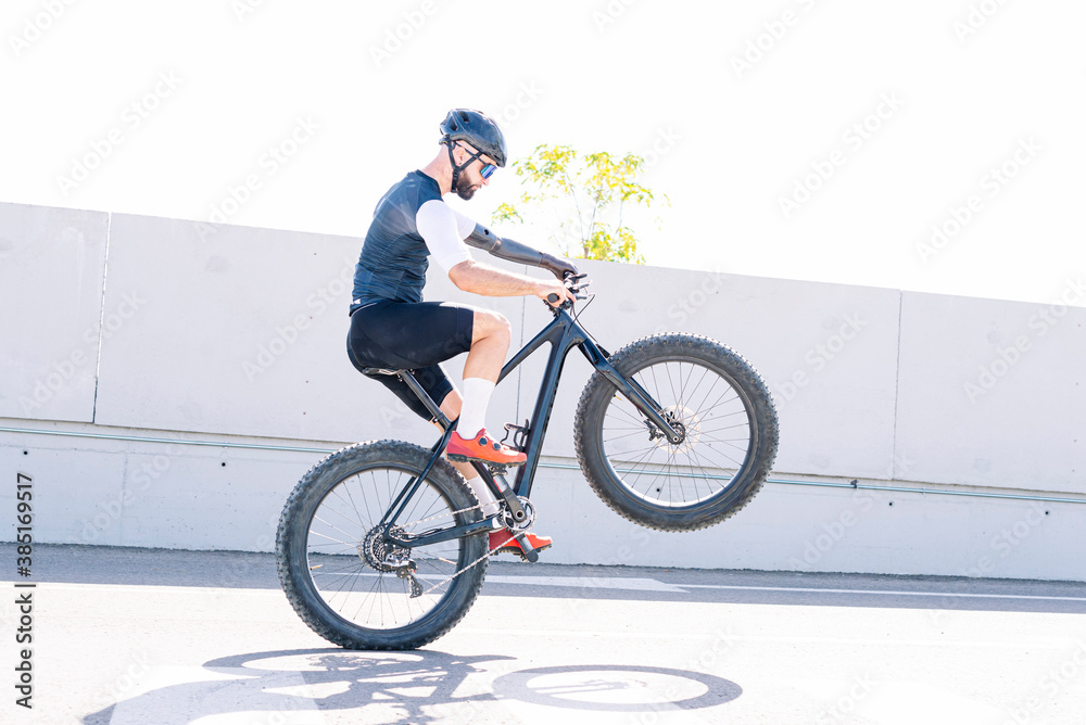 Male amputee athlete performing stunt with bicycle on road against clear sky Male amputee athlete performing stunt with bicycle on road against clear sky