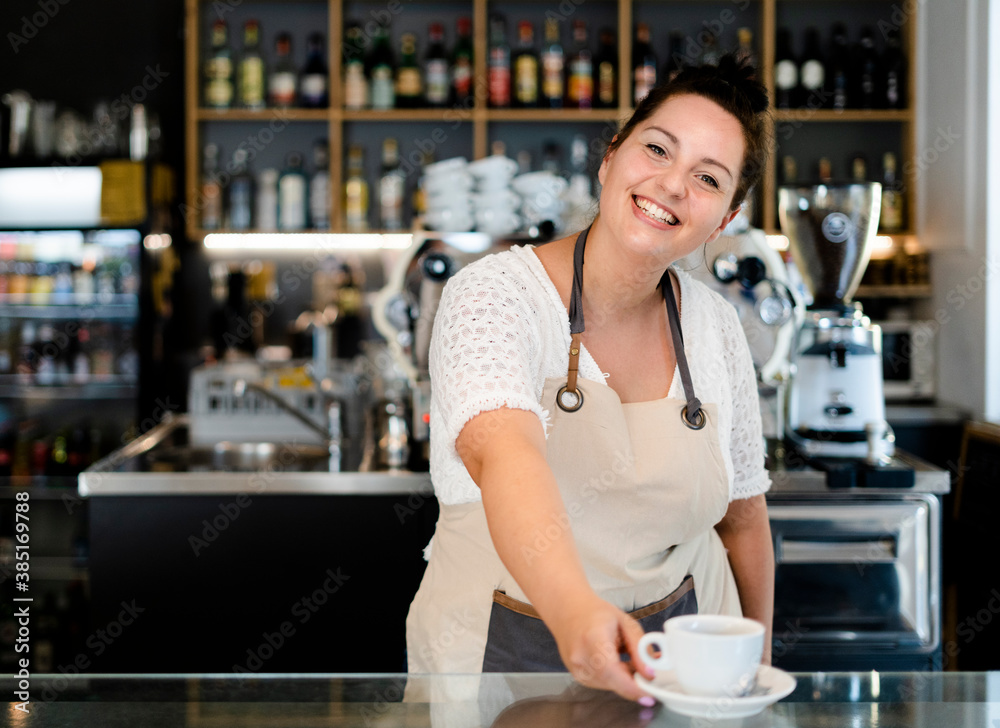 Smiling female owner serving coffee cup on bar counter while working in cafe Smiling female owner serving coffee cup on bar counter while working in cafe