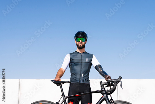 Male amputee cyclist with bicycle standing against clear blue sky