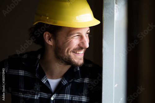 Close-up of smiling construction worker wearing helmet looking away by wall in house