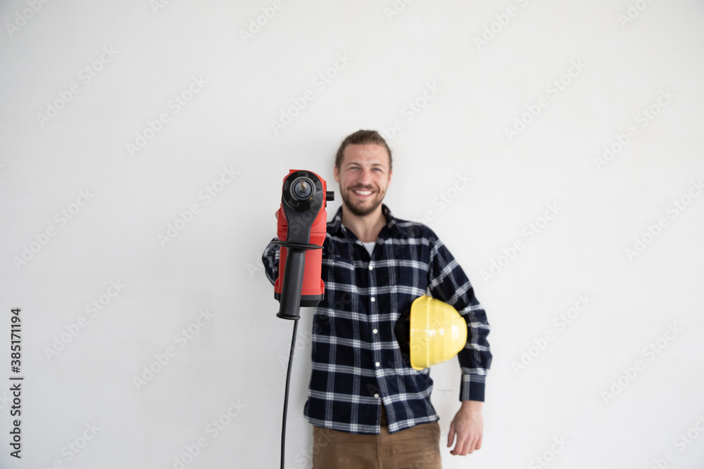 © MiJo/Westend61 - Smiling male worker holding work tool and helmet while standing against wall in house
