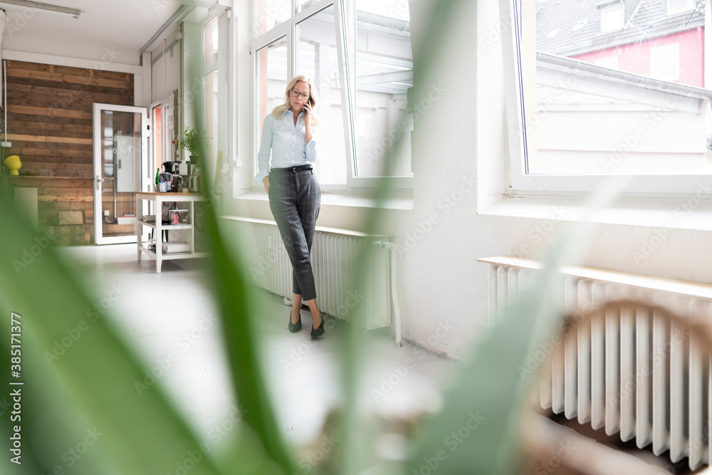Female professional talking over smart phone while standing by window at home Female professional talking over smart phone while standing by window at home