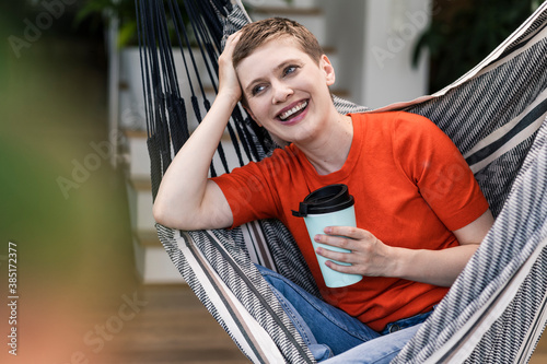 Cheerful mid adult woman holding coffee cup while sitting on swing in porch photo