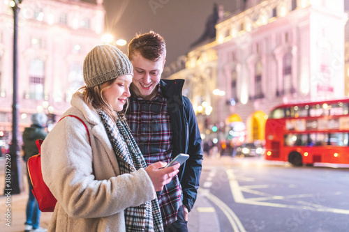 Woman using smart phone while standing with boyfriend in Piccadilly Circus at night photo