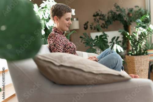 Mid adult woman with short hair using laptop while relaxing on sofa at home