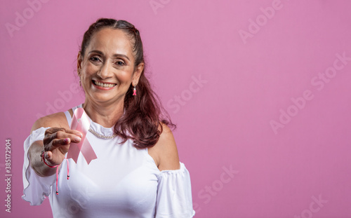 Mujer madura mostrando un lazo color rosa en un fondo rosado  photo