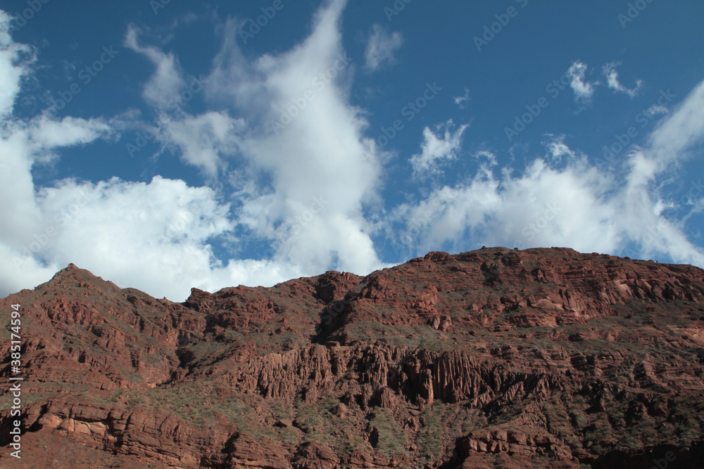 Panorama view of the brown rocky mountain peak and cliffs in the desert, under a blue sky. 