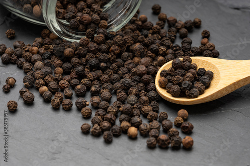 Close up of Black pepper with wooden spoon on black stone background