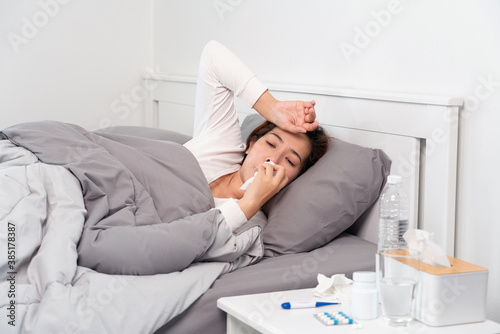 Sick Asian woman with cold sleeping on bed at home with high fever suffering from insomnia and medicine in foreground