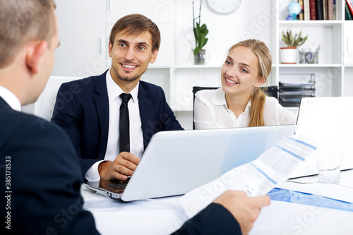 Three cheerful business colleagues discussing paper work with document in hands in office
