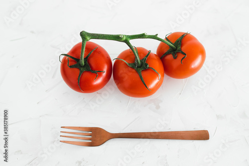 whole food diet concept, close-up of three tomatoes on vine with fork next to them on white minimalist background