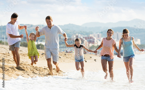 Portrait of smiling man and woman with four kids having fun and running on sandy beach together