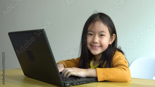 Cute Little Girl Uses Laptop While Sitting at the Desk in the Living Room. Child Doing Homework on Computer, Browses Through Internet