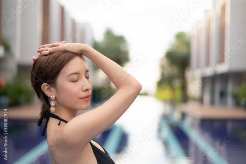 Asian woman in the black bikini posing near the swimming pool.