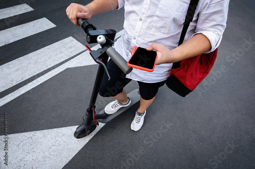 The guy holds a mobile phone in his hands while riding an electric scooter. Application for rent and geolocation of a scooter.